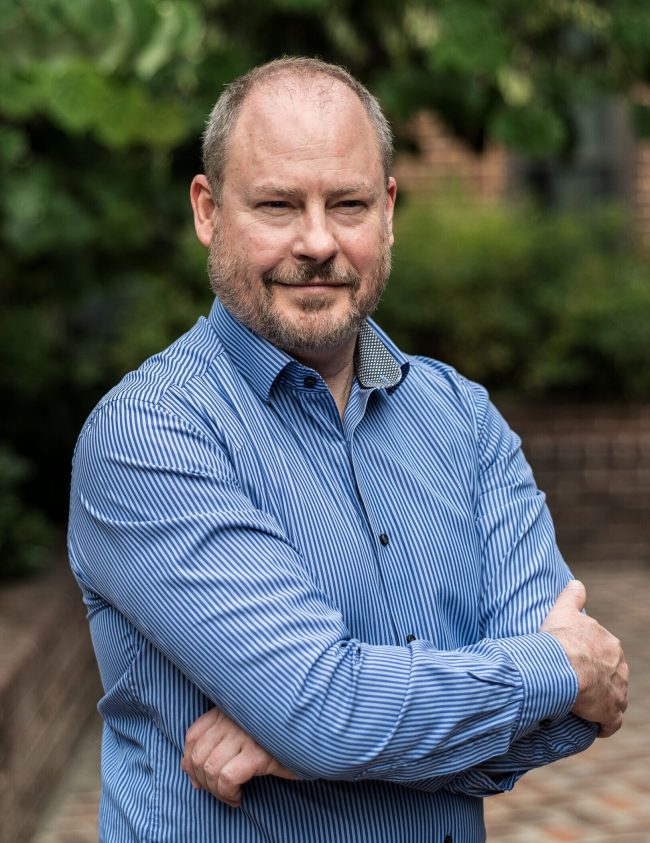 Sean Carberry standing in a courtyard with trees behind.