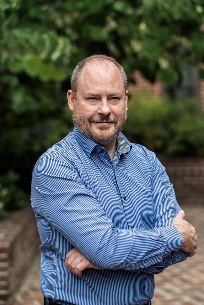 Sean Carberry standing in a courtyard with trees behind.